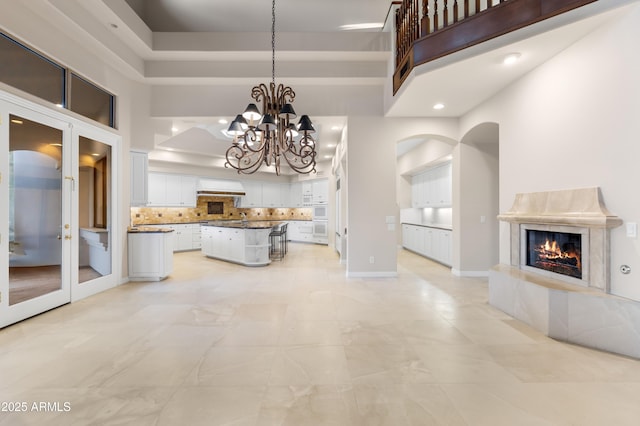 unfurnished living room featuring a high ceiling, a fireplace, a chandelier, baseboards, and french doors