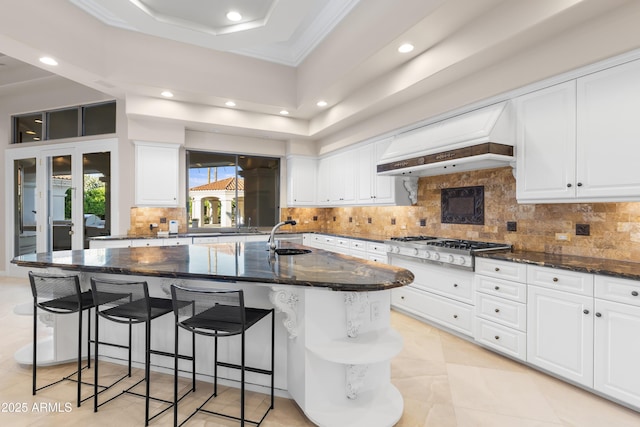 kitchen featuring custom exhaust hood, a sink, dark stone countertops, recessed lighting, and white cabinetry