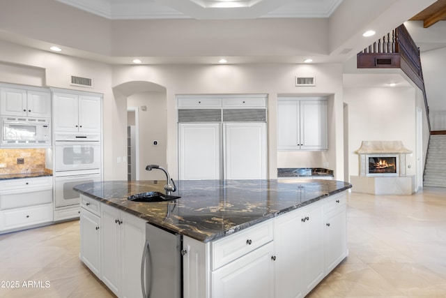 kitchen with a sink, white appliances, recessed lighting, arched walkways, and white cabinets