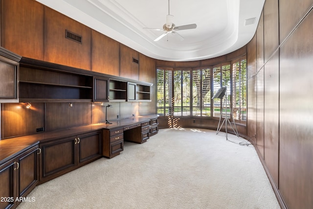 unfurnished office with built in desk, light colored carpet, ceiling fan, and plenty of natural light