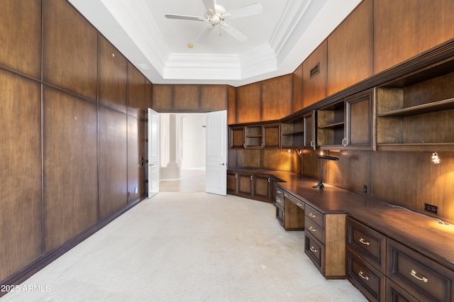 unfurnished office featuring built in desk, a raised ceiling, ceiling fan, ornamental molding, and light carpet
