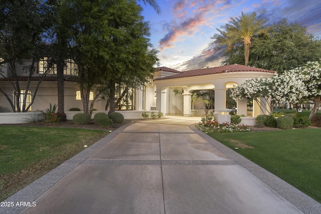 view of front of property featuring stucco siding, a front yard, a tiled roof, and driveway
