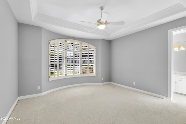 empty room featuring a tray ceiling, carpet floors, crown molding, a ceiling fan, and baseboards