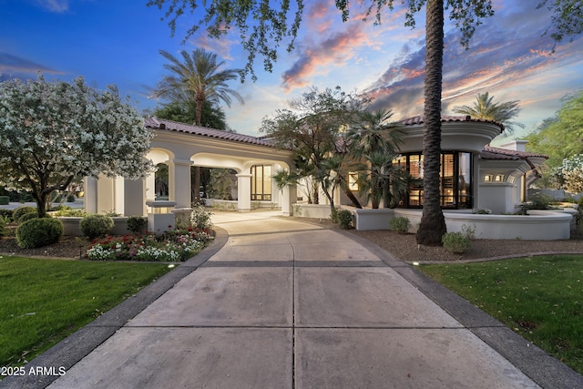 view of front facade featuring a tiled roof, stucco siding, a lawn, and driveway