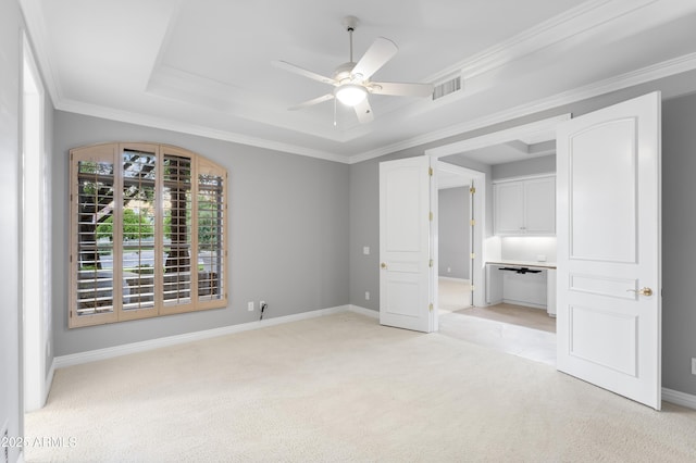 unfurnished bedroom featuring light colored carpet, a tray ceiling, baseboards, ornamental molding, and ceiling fan
