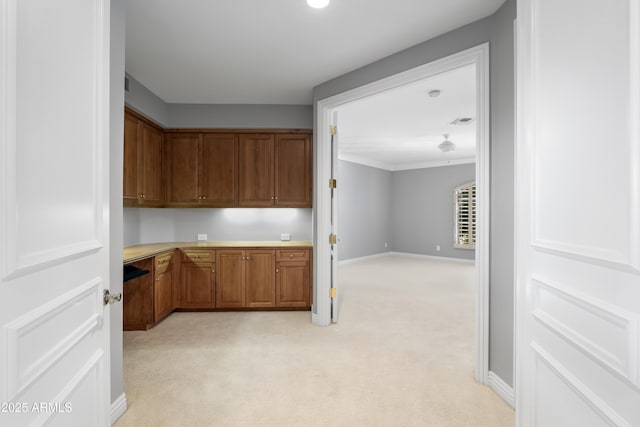 kitchen with light carpet, brown cabinetry, light countertops, and baseboards