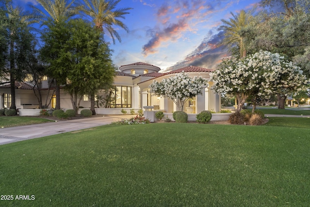 mediterranean / spanish house with a tile roof, a front yard, and stucco siding