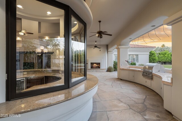 view of patio with an outdoor kitchen, grilling area, a lit fireplace, and ceiling fan