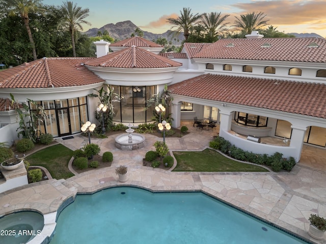 back of house with a patio area, a tile roof, stucco siding, a mountain view, and a chimney