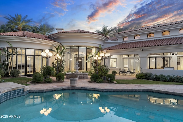 back of house at dusk featuring a patio, stucco siding, and an outdoor pool