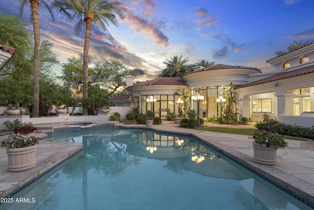 pool at dusk featuring a patio area and a pool with connected hot tub
