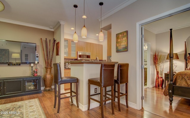 6900 E Princess Dr Unit 1176, Phoenix, AZ 85054 - kitchen with stainless steel microwave, a breakfast bar, wood finished floors, glass insert cabinets, and crown molding