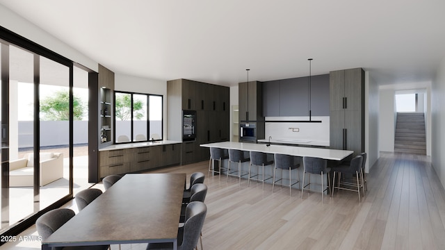 kitchen with a breakfast bar, hanging light fixtures, a center island with sink, and light hardwood / wood-style flooring