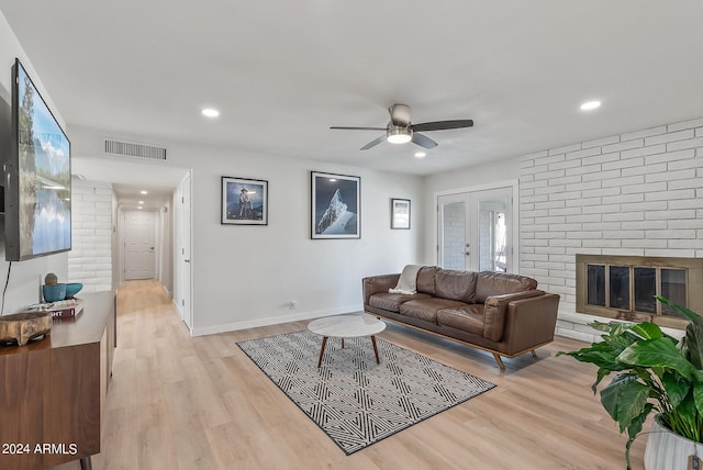 living room with light wood-type flooring, a brick fireplace, french doors, and ceiling fan