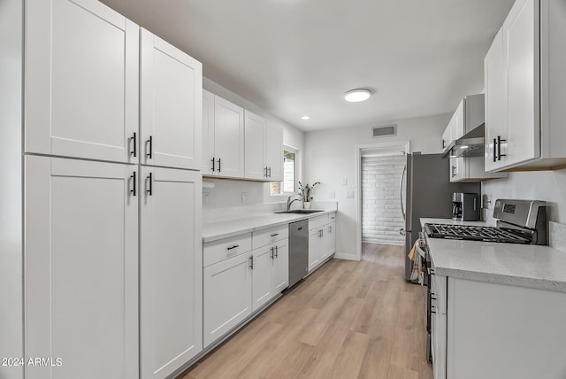 kitchen with white cabinetry, wall chimney range hood, stainless steel appliances, sink, and light wood-type flooring