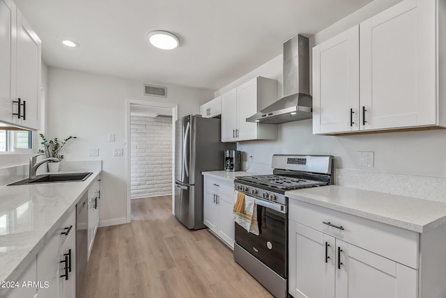 kitchen with sink, white cabinetry, light stone countertops, appliances with stainless steel finishes, and wall chimney exhaust hood