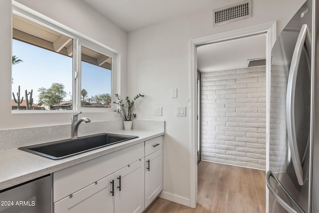 kitchen with white cabinetry, dishwashing machine, stainless steel refrigerator, light hardwood / wood-style flooring, and sink