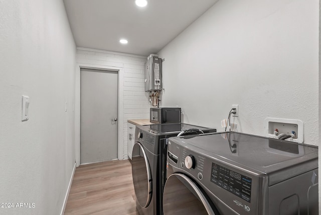 clothes washing area featuring water heater, washer and dryer, and light hardwood / wood-style flooring