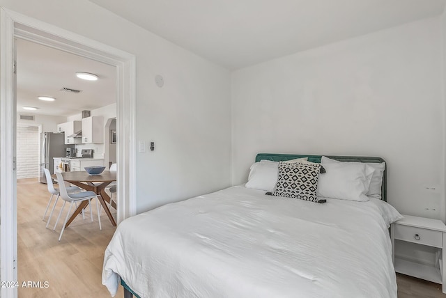 bedroom with stainless steel fridge and light wood-type flooring