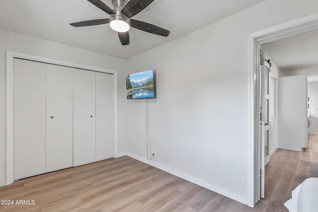 unfurnished bedroom with ceiling fan, a closet, a barn door, and light hardwood / wood-style flooring