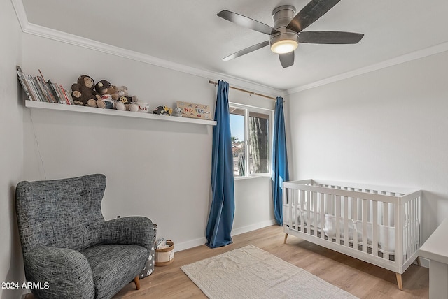 bedroom featuring ceiling fan, ornamental molding, wood-type flooring, and a crib