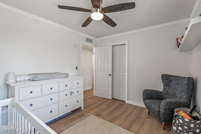 bedroom featuring ceiling fan, a nursery area, crown molding, light wood-type flooring, and a closet