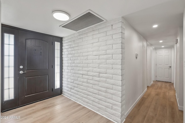 entrance foyer with brick wall and light hardwood / wood-style flooring