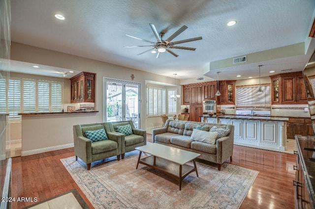 living room featuring ceiling fan, sink, and light wood-type flooring