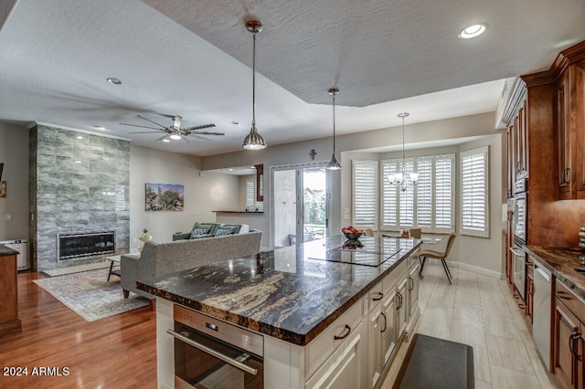 kitchen with appliances with stainless steel finishes, a fireplace, a center island, dark stone countertops, and light hardwood / wood-style flooring