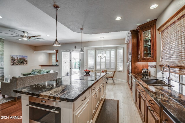 kitchen with dark stone counters, light wood-type flooring, sink, ceiling fan with notable chandelier, and decorative light fixtures