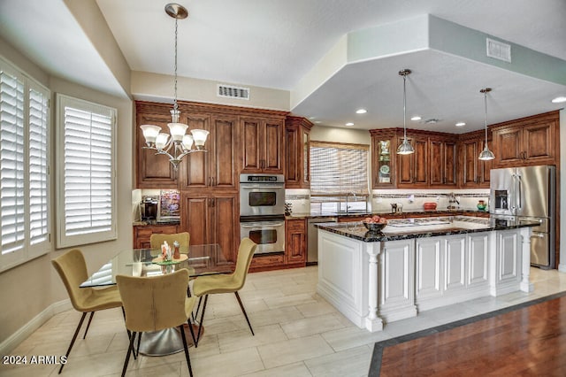 kitchen with appliances with stainless steel finishes, sink, a center island, decorative light fixtures, and dark stone counters