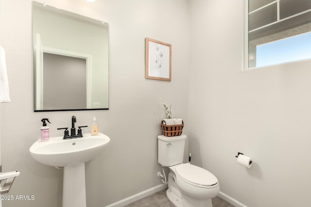 half bath featuring baseboards, a sink, and toilet