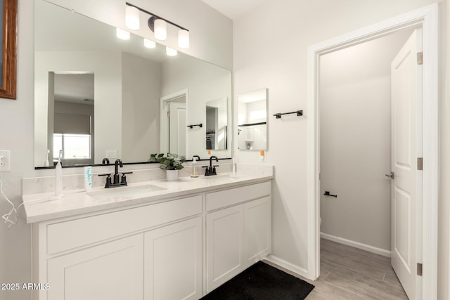 bathroom featuring double vanity, wood finished floors, a sink, and baseboards