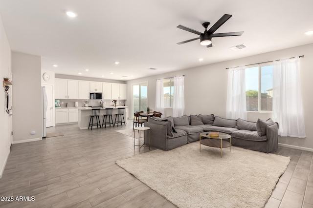 living area featuring visible vents, ceiling fan, a wealth of natural light, and light wood-style floors