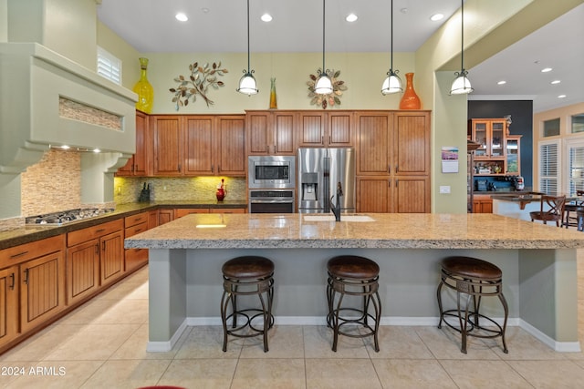 kitchen featuring light tile patterned floors, appliances with stainless steel finishes, a kitchen breakfast bar, an island with sink, and decorative backsplash