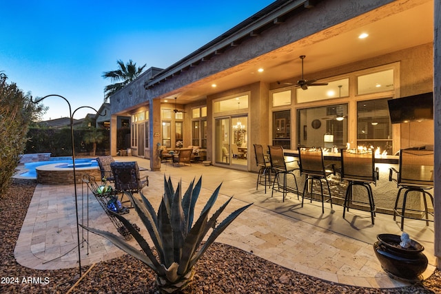 patio terrace at dusk with a pool with hot tub, ceiling fan, and exterior bar