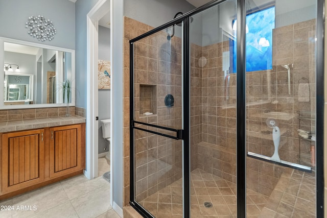 bathroom featuring a shower with door, vanity, tile patterned floors, and toilet