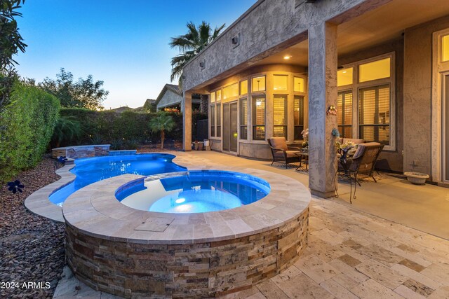 pool at dusk with a patio area, pool water feature, and an in ground hot tub