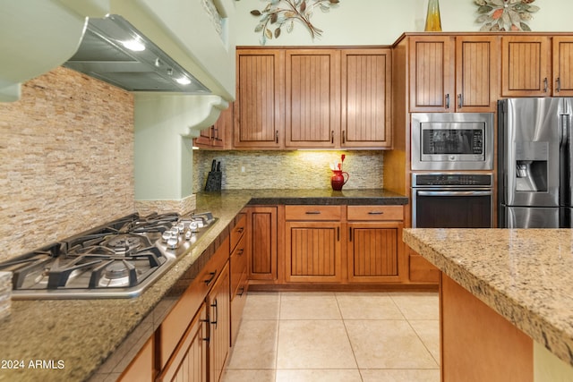 kitchen with light tile patterned floors, appliances with stainless steel finishes, custom range hood, light stone countertops, and decorative backsplash