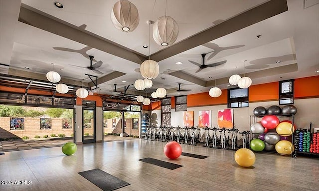 exercise room with hardwood / wood-style floors, a tray ceiling, and ceiling fan