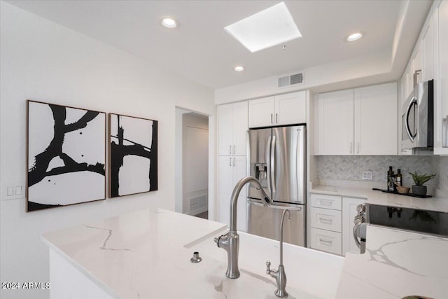 7222 E Gainey Ranch Rd Unit 241, Scottsdale, AZ 85258 - kitchen with appliances with stainless steel finishes, white cabinets, tasteful backsplash, light stone countertops, and recessed lighting