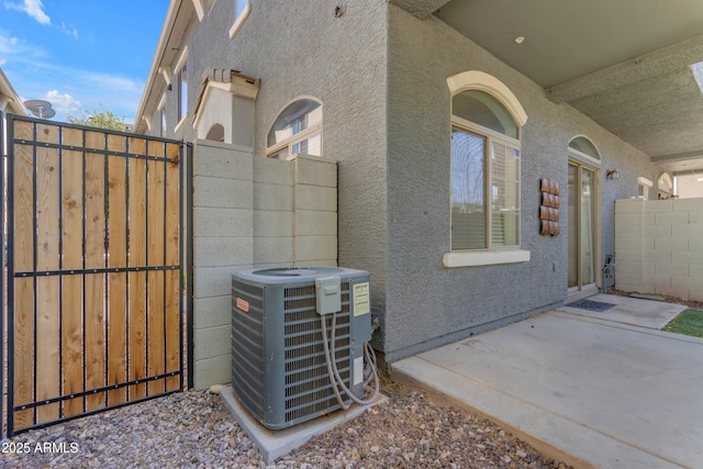 view of side of home with central air condition unit, stucco siding, a gate, and a patio area