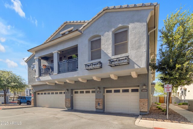 view of property featuring an attached garage, stucco siding, driveway, and a balcony