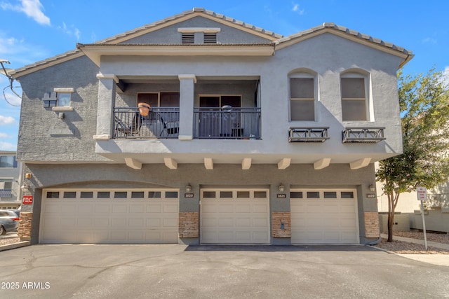 view of front of house featuring an attached garage, a balcony, asphalt driveway, and stucco siding