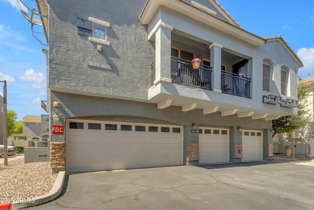 view of front of property featuring a balcony, an attached garage, stucco siding, and driveway