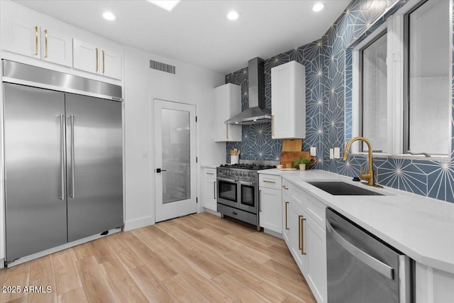 kitchen with premium appliances, visible vents, light countertops, a sink, and wall chimney range hood