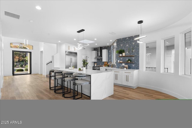 kitchen with wall chimney exhaust hood, open shelves, visible vents, white cabinetry, and built in refrigerator