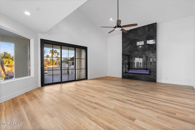 unfurnished living room with ceiling fan, high vaulted ceiling, a fireplace, baseboards, and light wood-style floors