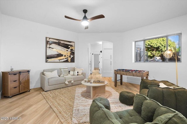 living area with arched walkways, light wood-style flooring, and a ceiling fan