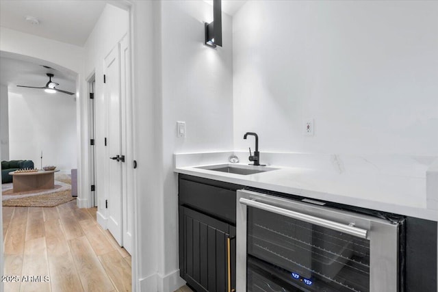 kitchen with a ceiling fan, wine cooler, light countertops, light wood-style floors, and a sink